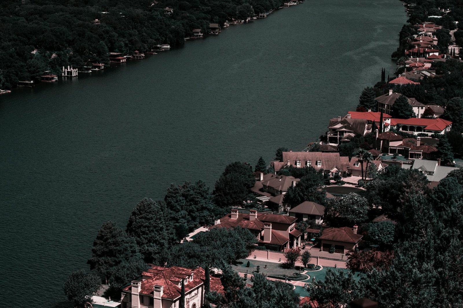 Aerial view of elegant homes along a tranquil river surrounded by lush greenery, showcasing affluence and scenic beauty.