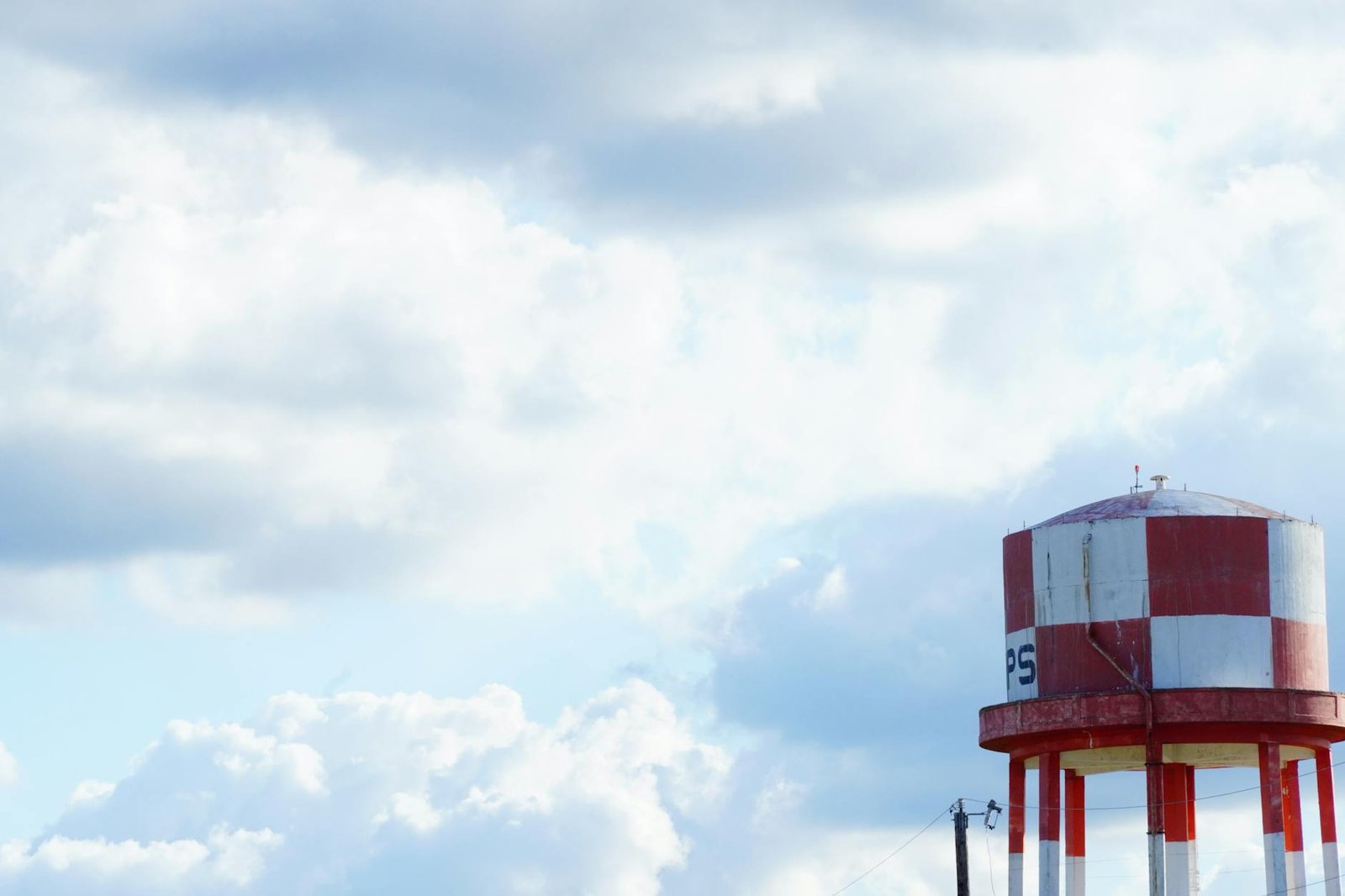 A scenic view of a red and white water tower under a blue, cloudy sky in San Marcos, Texas.