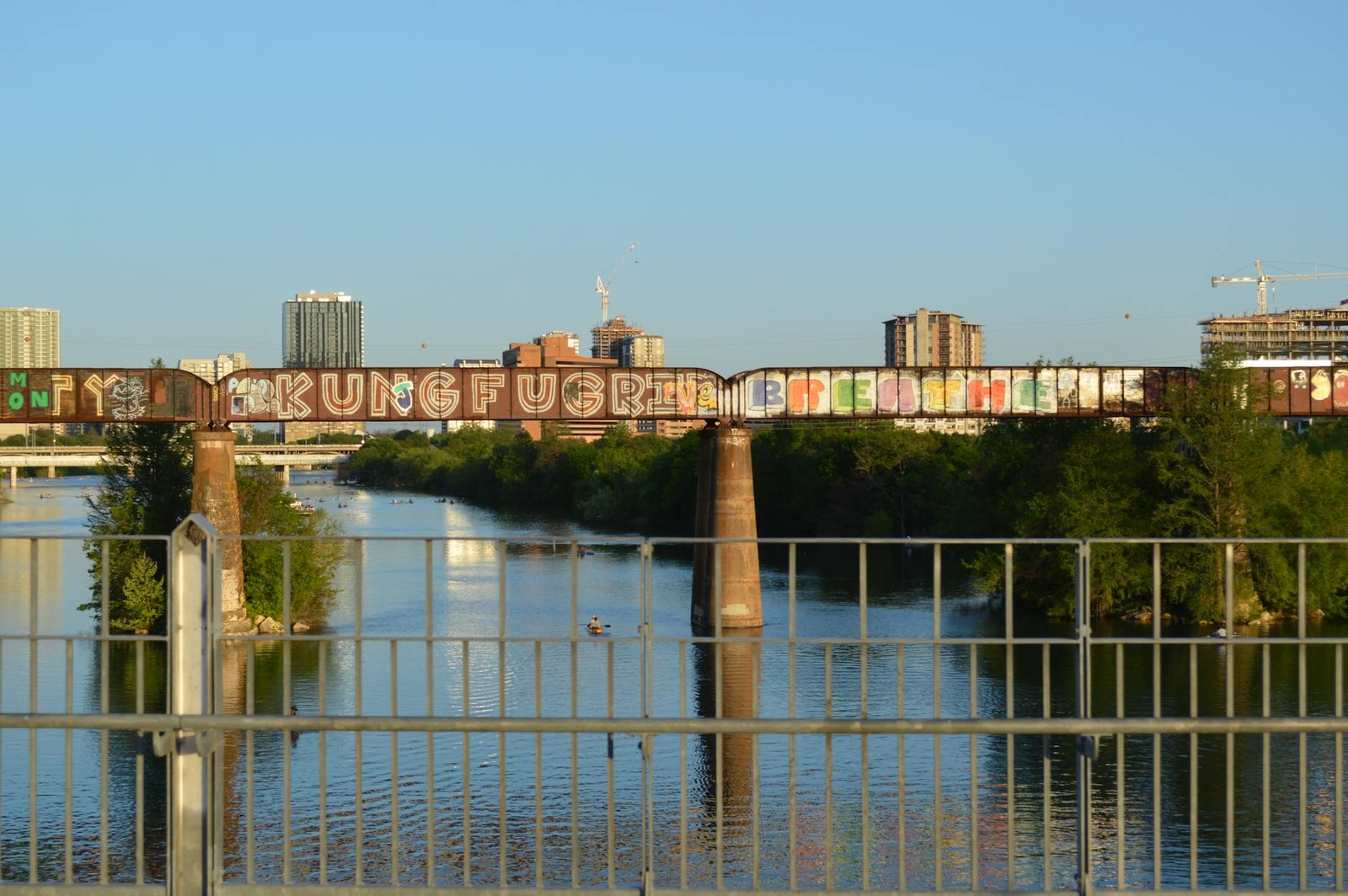 Colorful graffiti on a bridge over Lady Bird Lake with Austin skyline in the backdrop.