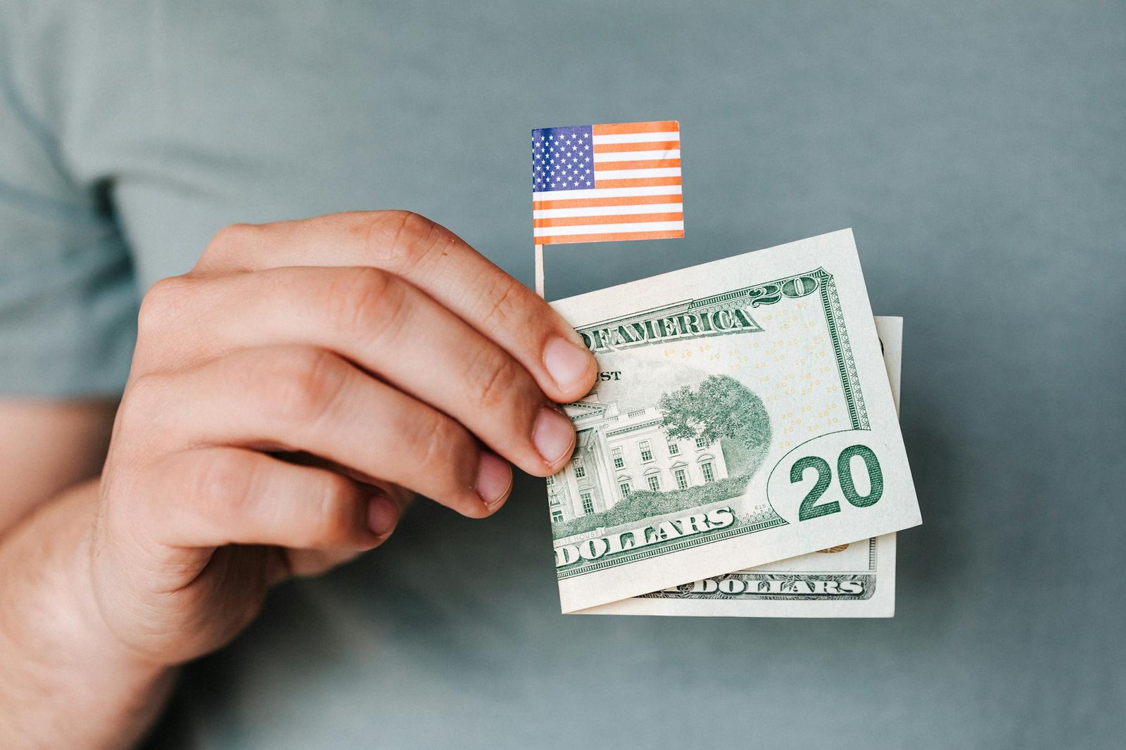 Crop anonymous man demonstrating small paper United States flag and folded twenty dollar banknote