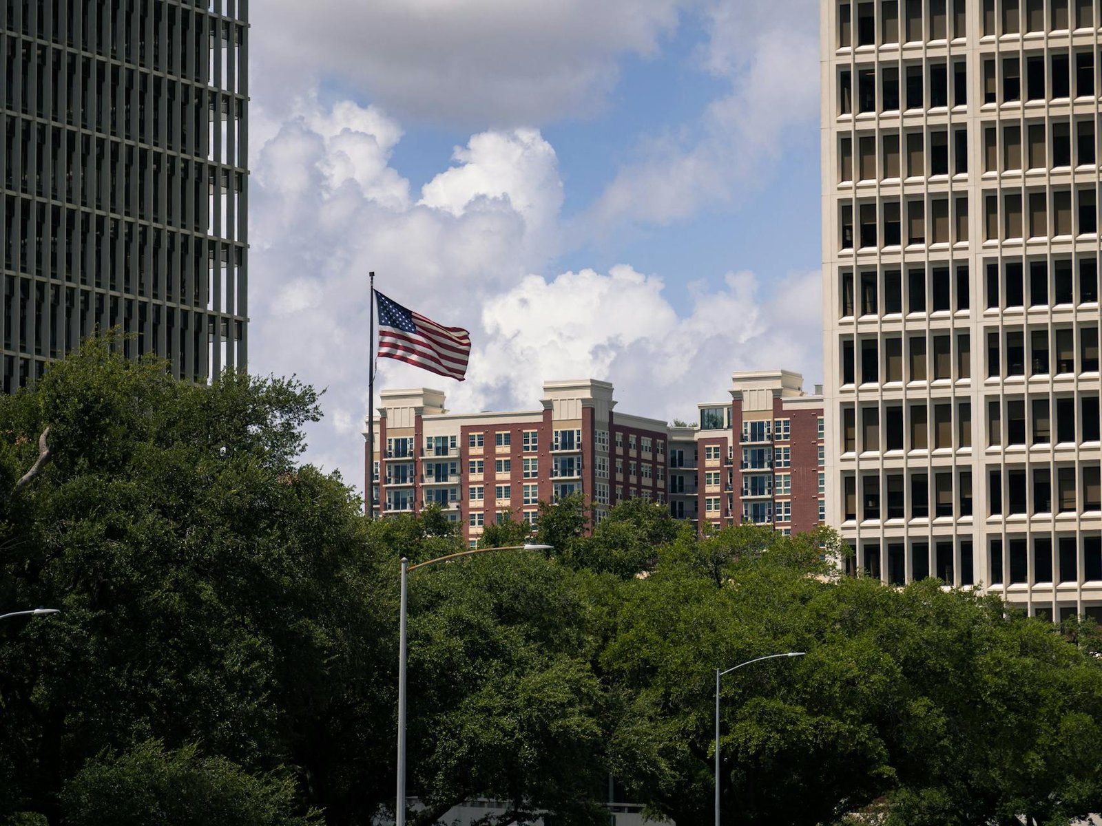 American flag waving between Houston skyscrapers on a sunny day.
